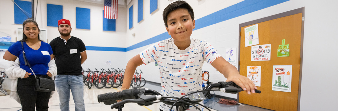 student and parents holding bikes in gymnasium 