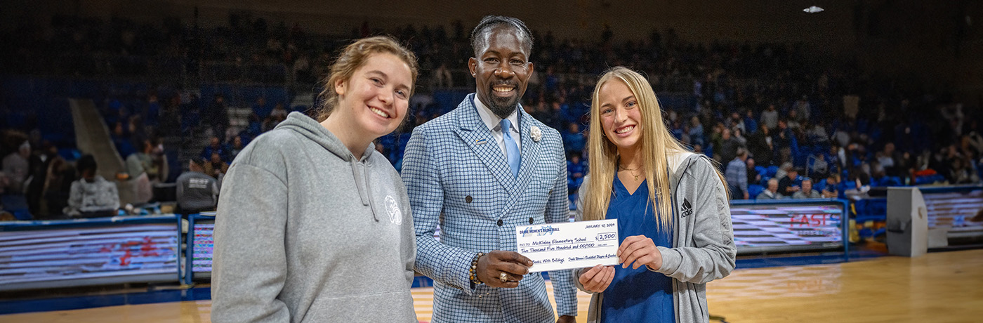 Dr. Ian Roberts holding a check for McKinley teachers on drake basketball court